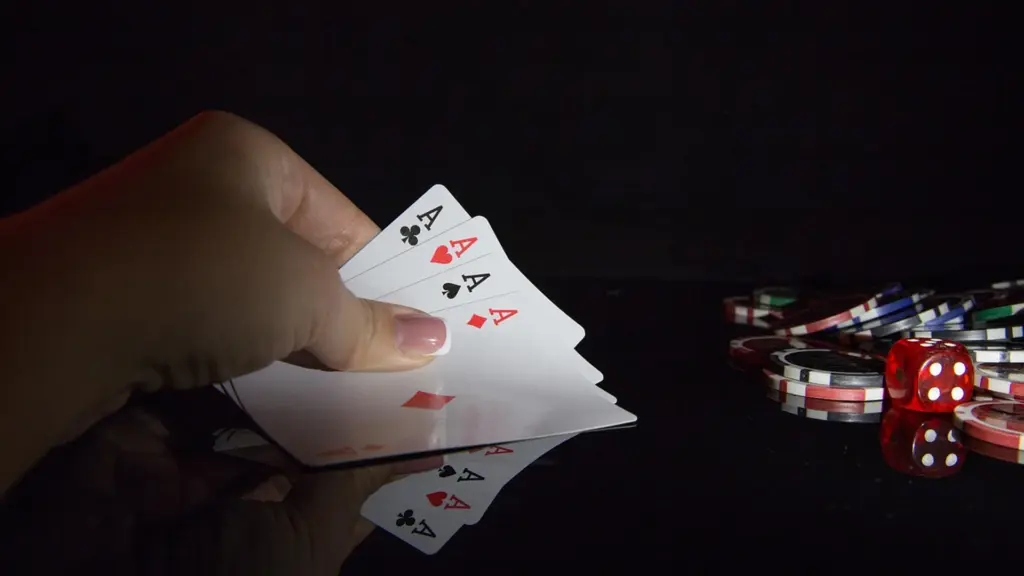 Een hand die vier aas-kaarten vasthoudt naast casino chips en rode dobbelstenen op een donkere ondergrond.