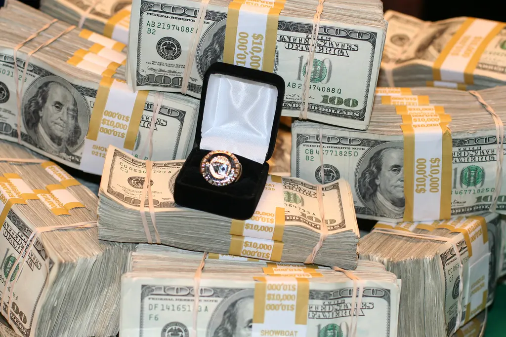 Een gouden kampioenschapsring van de World Series of Poker Circuit in een zwart doosje, omringd door stapels dollarbiljetten.